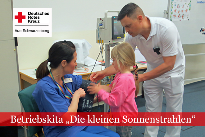 Kindergartenkind legt einer Pflegekraft eine Blutdruckmanschette an und wird von einem Pfleger unterstützt.