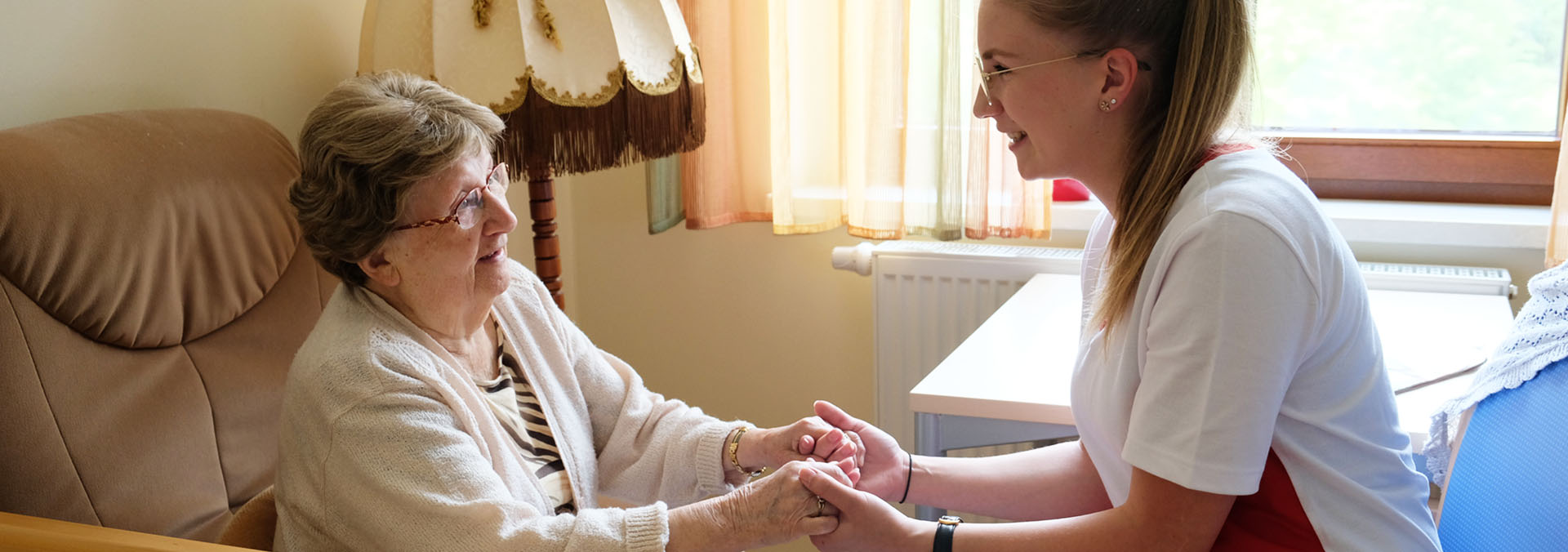 Mitarbeiterin hält Händchen mit Seniorin