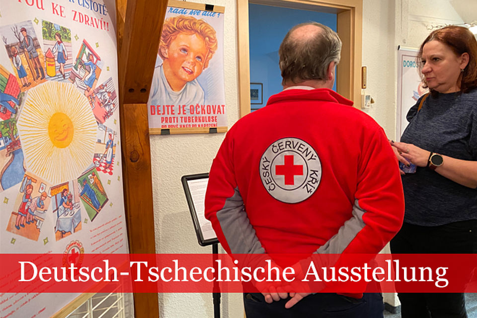 Museumsbesucher im Gespräch, Eine Person mit Logo des Tschechischen Roten Kreuzes auf dem Rücken der Jacke